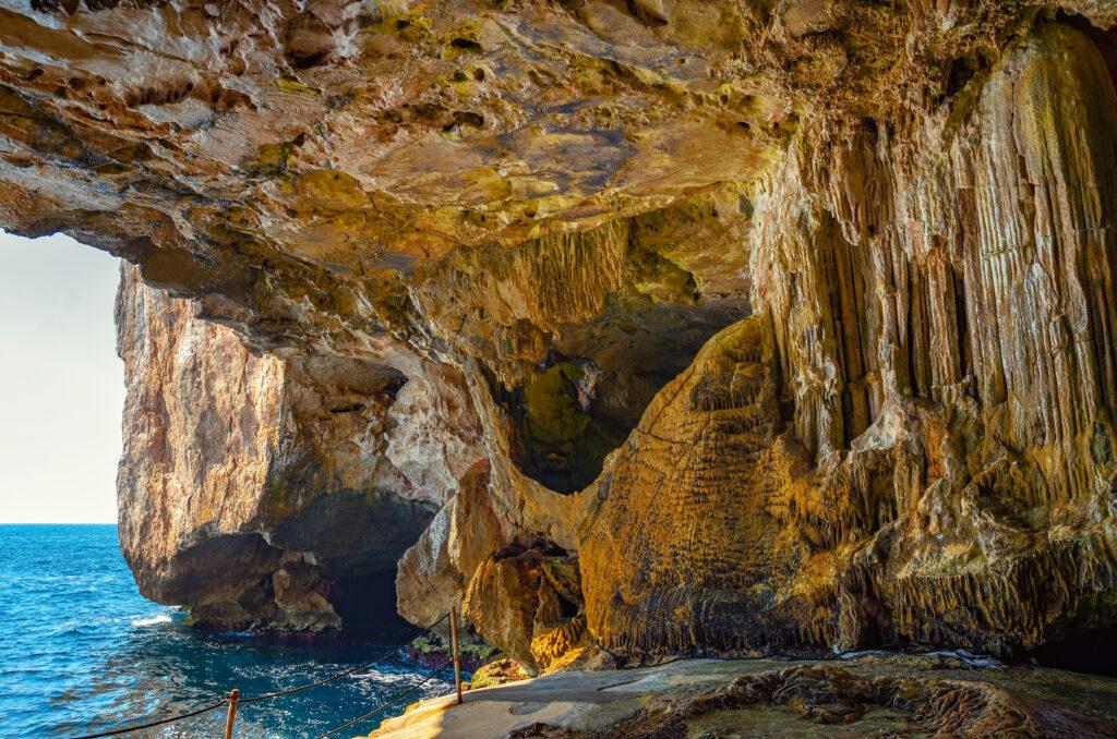 Interior of Neptune's Cave with stunning rock formations and a view of the Mediterranean Sea in Capo Caccia, Sardinia. This cave is also known as Neptune's Grotto, Sardinia - My Travel Monkey